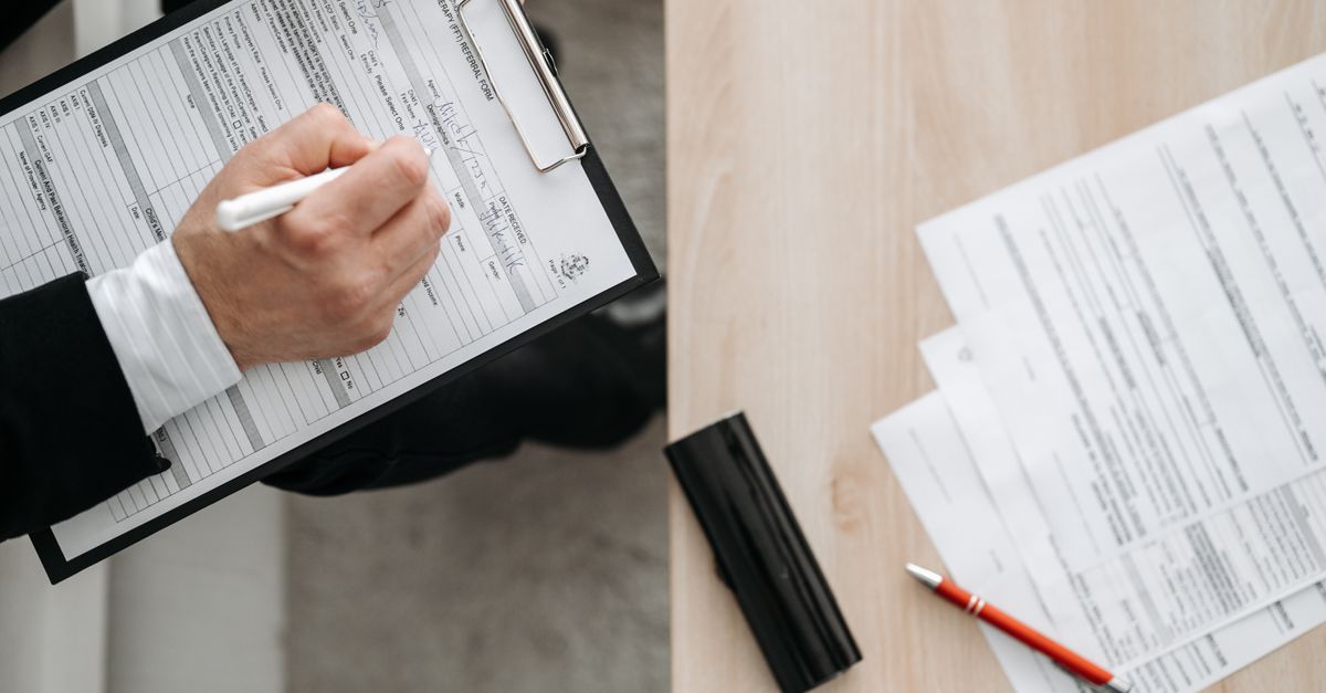 Adult filling out a vital statistics application form at a desk with a pen.