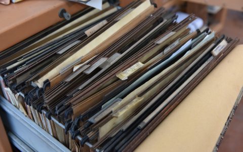 Close-up of hands organizing official government forms and documents on a wooden desk.