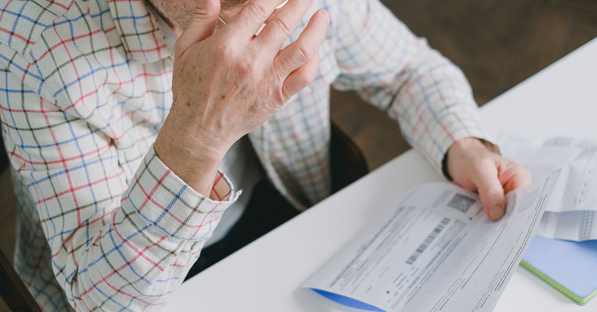 Close-up of a consumer reviewing an electric bill statement at a wooden desk.