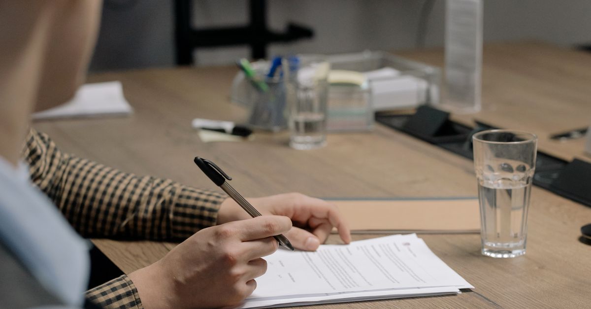 Hands signing an official corporate agreement on a wooden table.