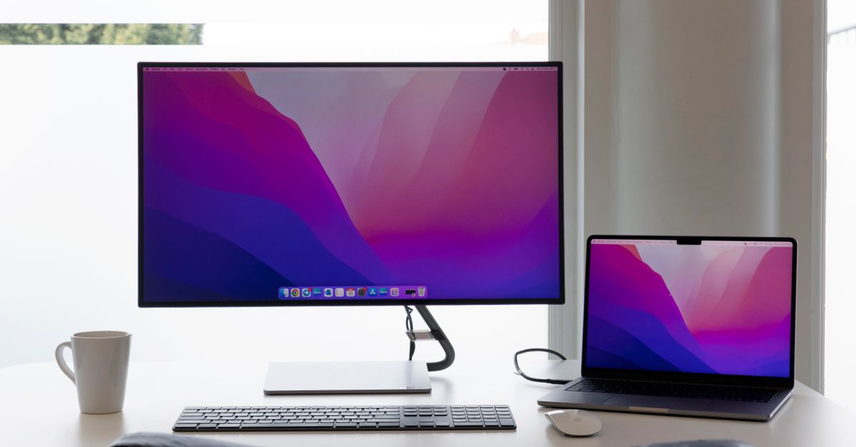 Laptop connected to external monitors displaying software code and spreadsheets.