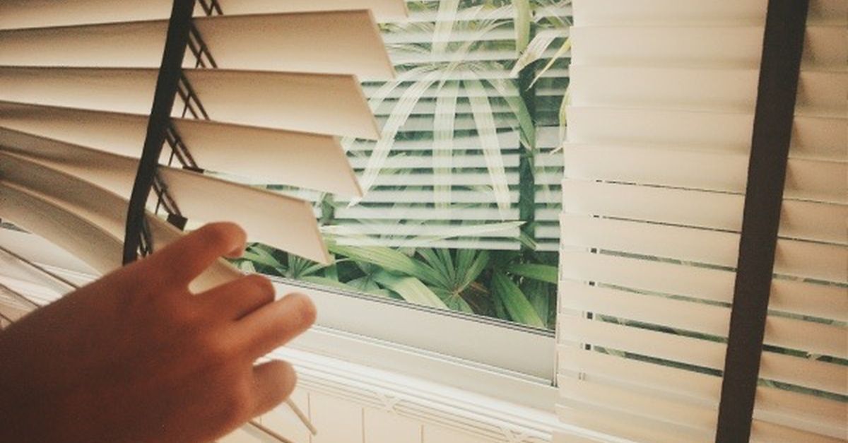 Homeowner adjusting horizontal slats on standard window blinds.