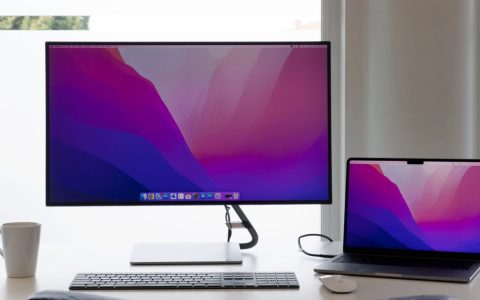 A portable dual monitor setup on a wooden desk in a bright room.