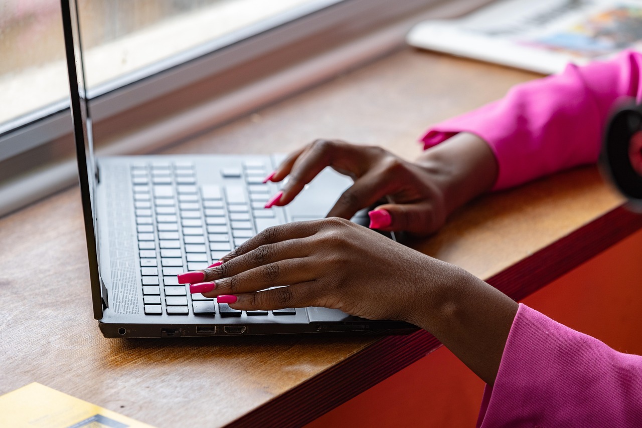 An office worker sitting at a desk with window blinds partially tilted shut.