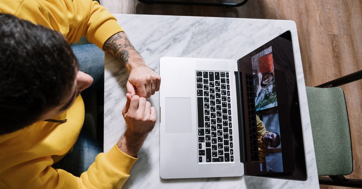 A pair of hands adjusting a laptop webcam shutter in a bright home office.