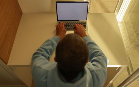 A laptop on a wooden desk fitted with a dark physical privacy screen filter.