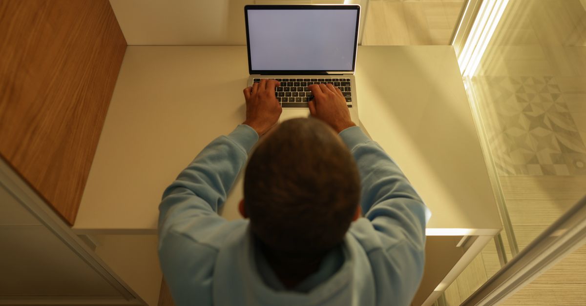A laptop on a wooden desk fitted with a dark physical privacy screen filter.