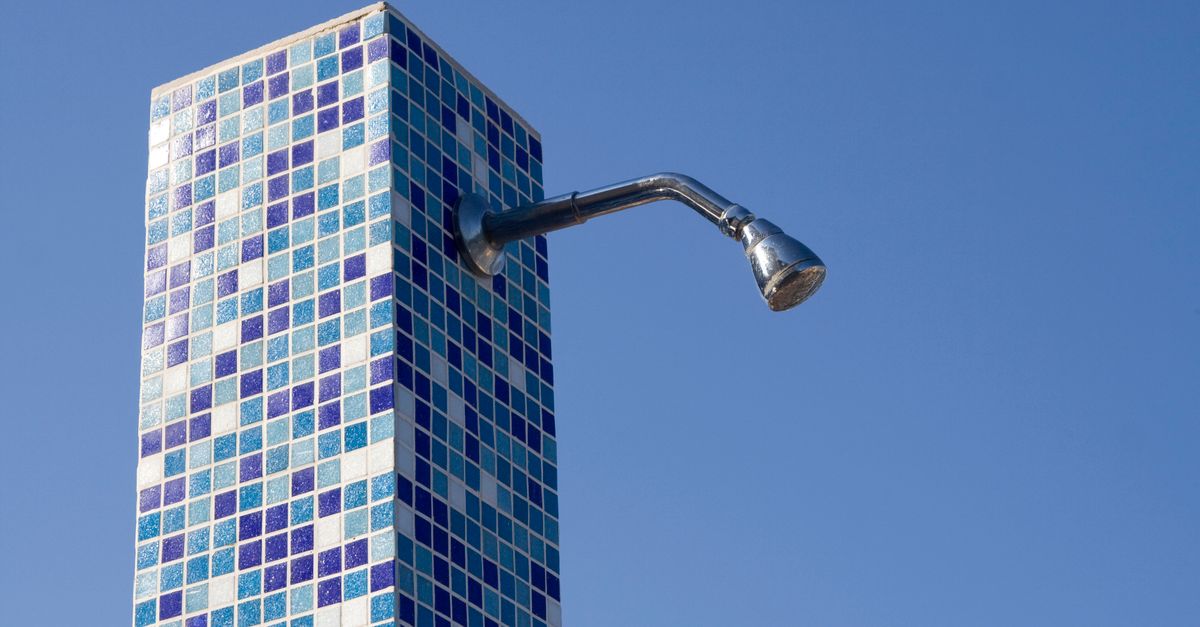 Water spraying from a clean chrome showerhead onto neutral tile walls