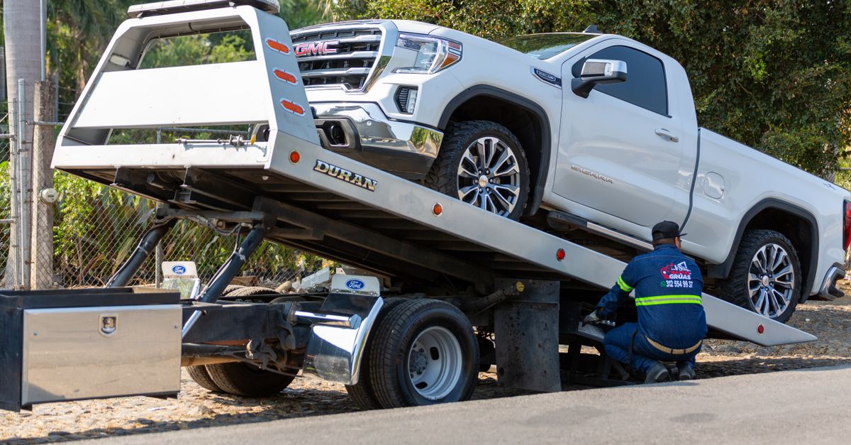 A person loading long wooden planks into the open bed of a compact pickup truck.