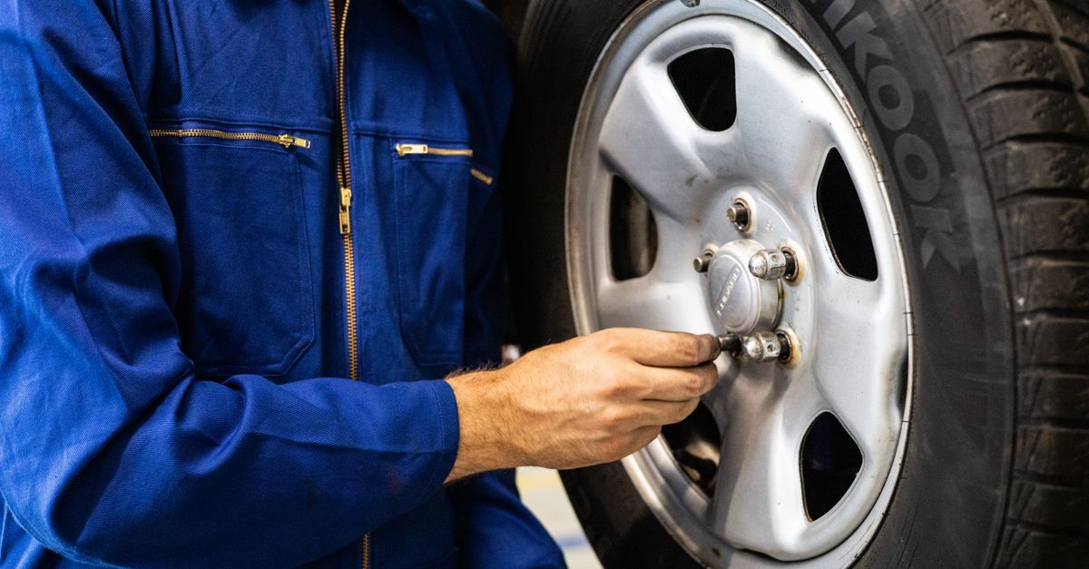 Auto mechanic checking tire tread depth in a service bay.