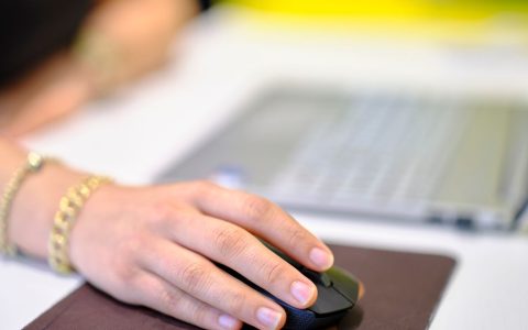 Close-up of a remote worker's hand gripping an ergonomic vertical mouse on a wooden desk.