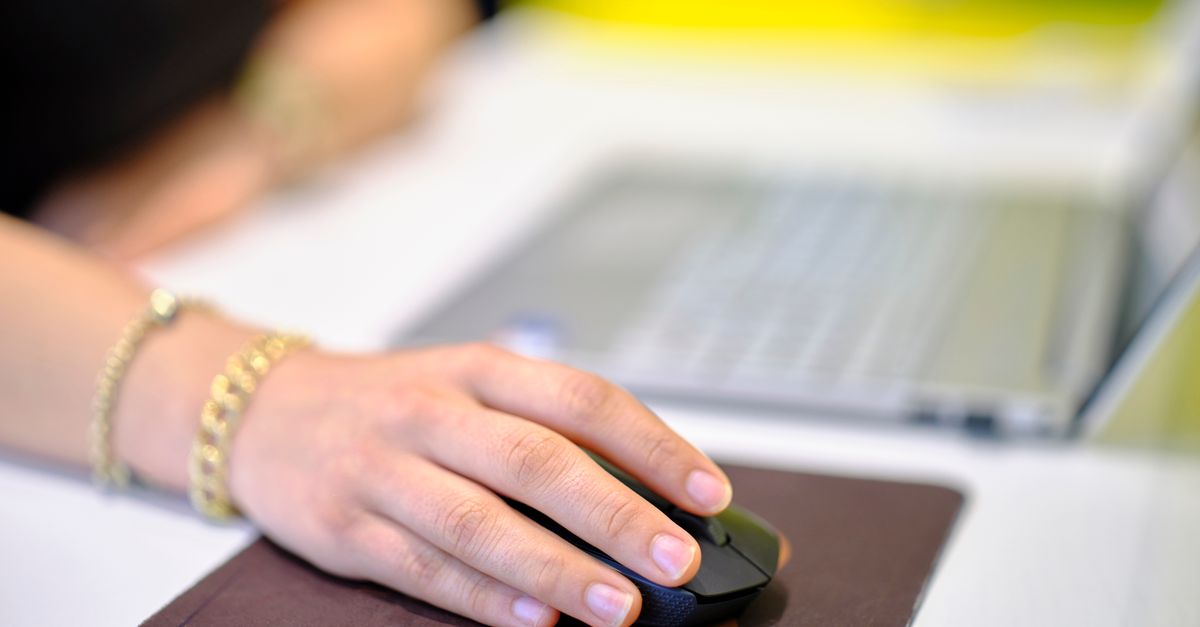 Close-up of a remote worker's hand gripping an ergonomic vertical mouse on a wooden desk.