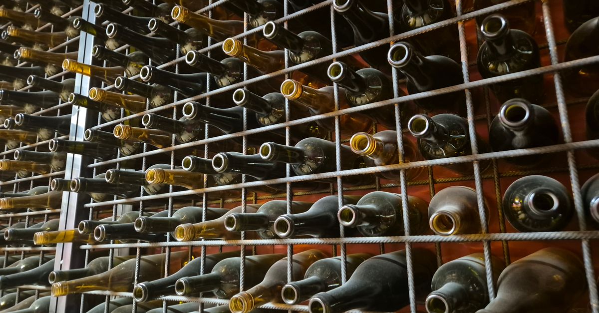 Close-up of wooden wine rack shelves inside a temperature-controlled cabinet filled with various wine vintages.